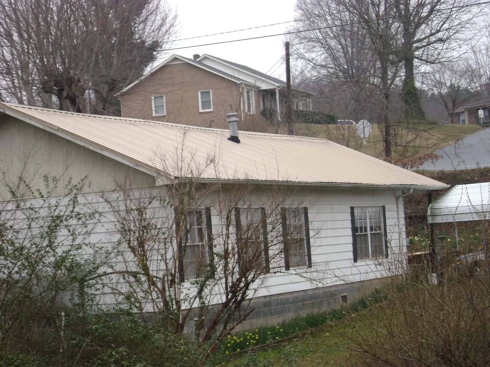 Tan metal roof on a white sided house set into a hillside — Commercial Roofing by Roofing Brothers in Webster